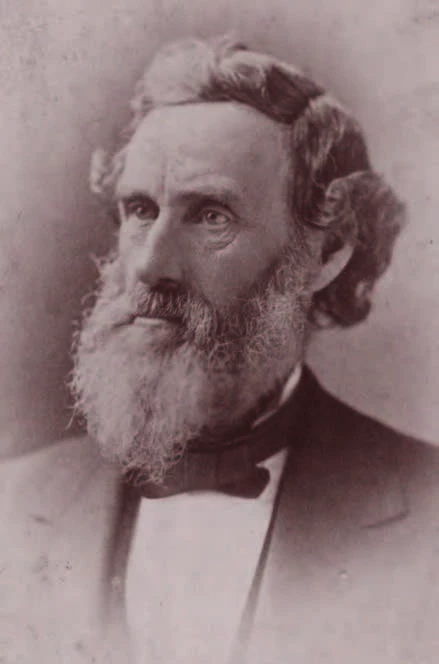 black and white photograph of a light skinned man with long wavy hair and a large beard.