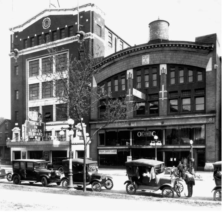 cars are parked along the street in front of the garage building. On the left is a new building, a theater, which is 6 stories tall.