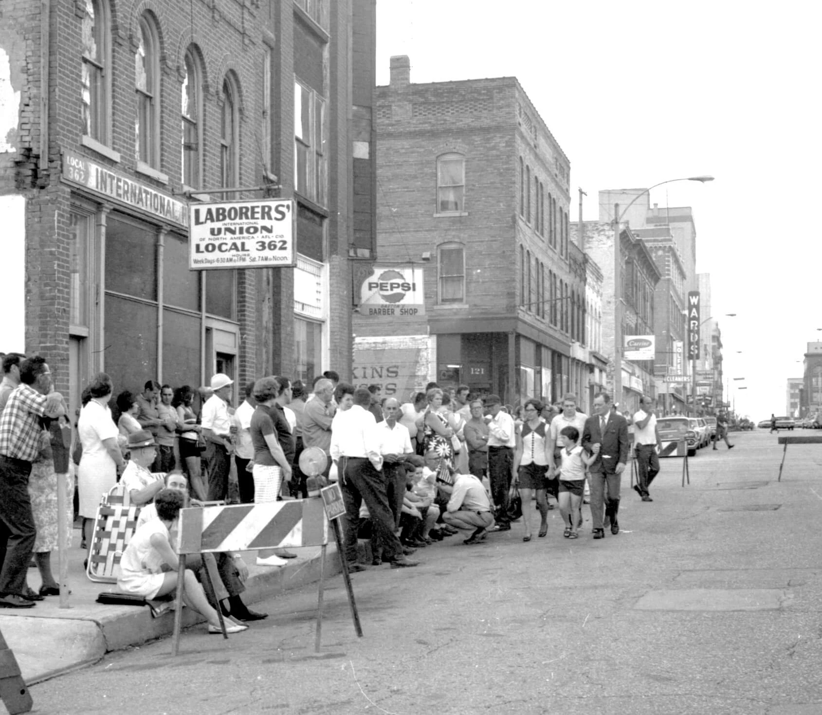 A crowd of people standing on a sidewalk in front of a brick building.