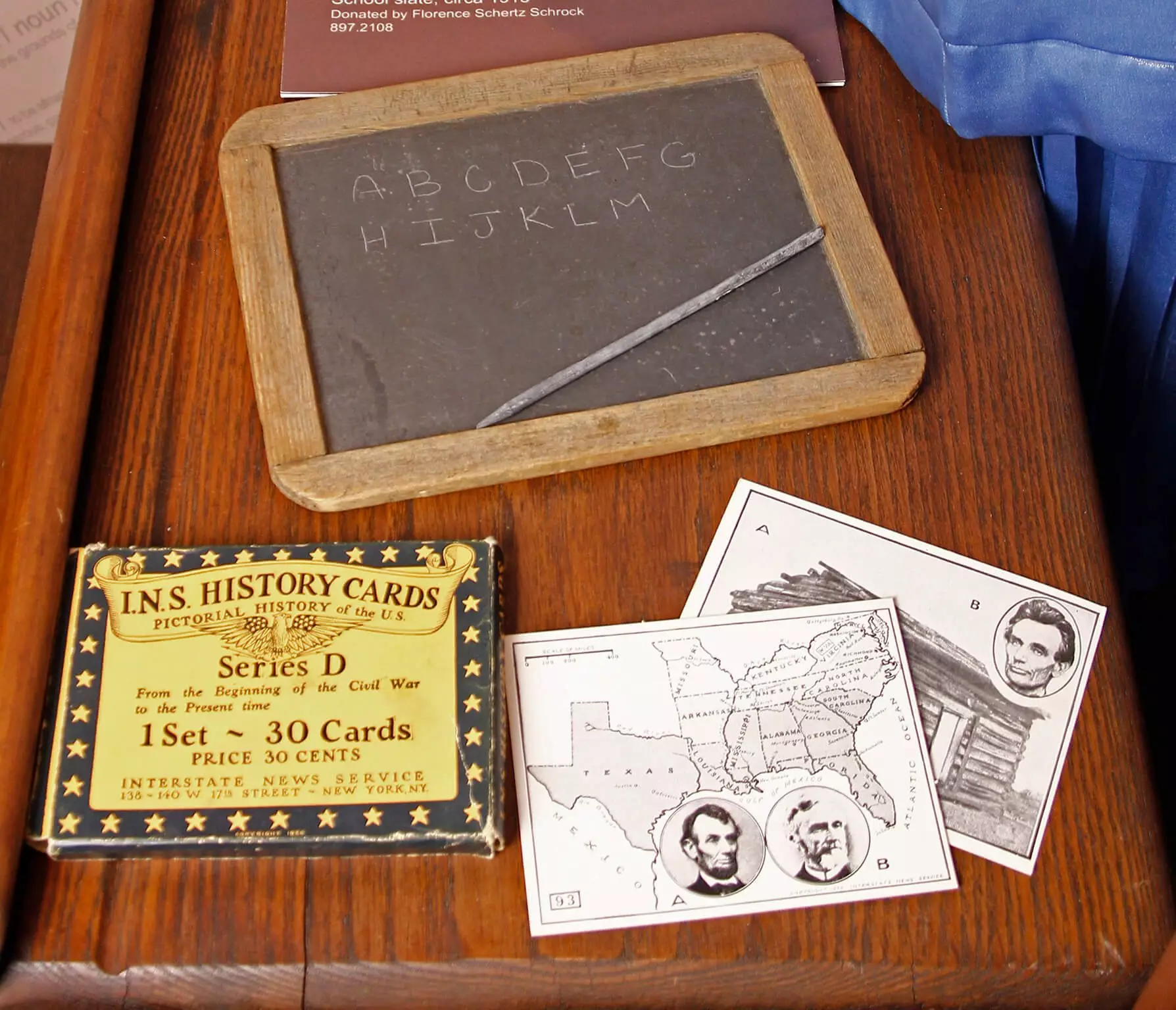 Small wooden framed slate board with half the alphabet written on it, sitting on a desk near a deck of I.N.S. history of the US flashcards