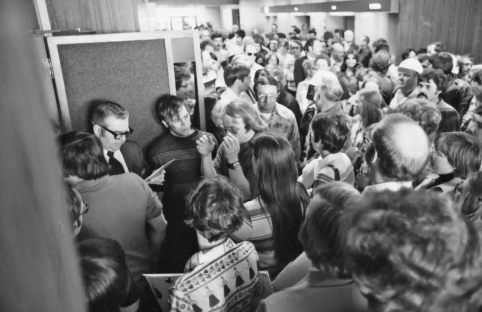 Photo of a crowd of mostly men attempting to enter through the door of a courtroom.