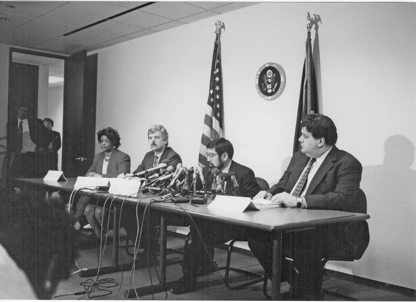 Five people in formal wear are sitting at a table with several microphones on it.