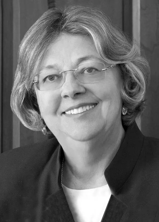 white woman smiles at the camera, she has chin-length light hair and glasses.