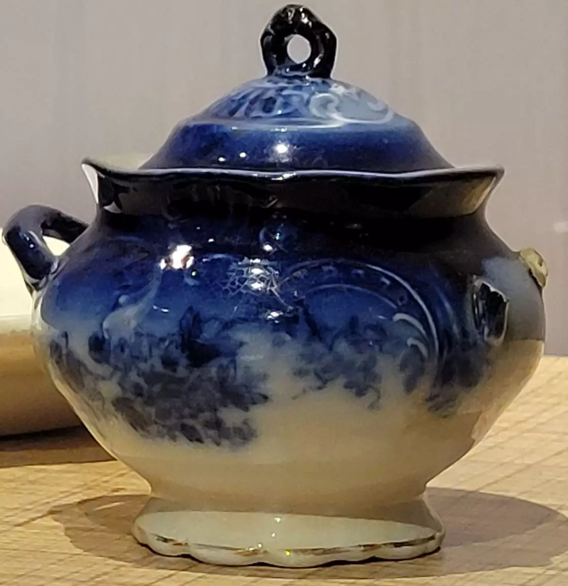 This bowl and lid is cobalt blue on top and fades to white with a delicate floral pattern in the middle. One of the handles has broken off.