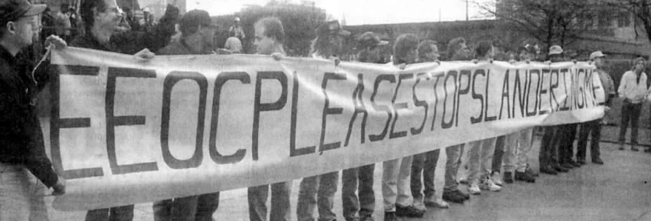 Black and white photograph of people standing in a line holding a banner.