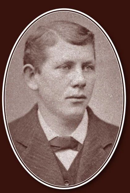 Portrait of a young man with wavy, side-parted hair, light colored eyes, and wearing a three-piece suit with bow tie.