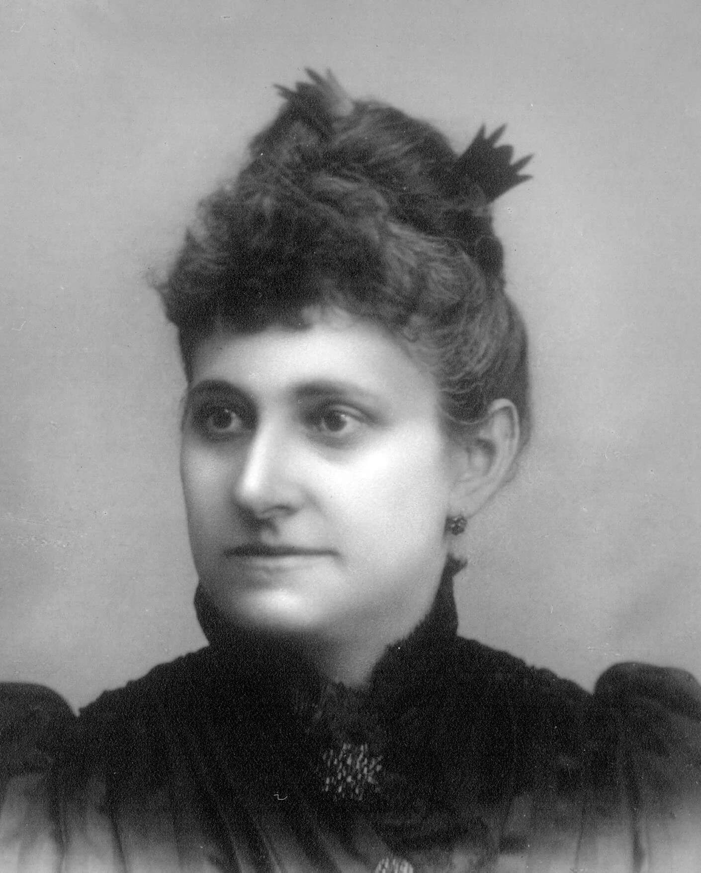 Black and white photo of a light-skinned woman with up high, puffed sleeves and a brooch pinned at her neck.