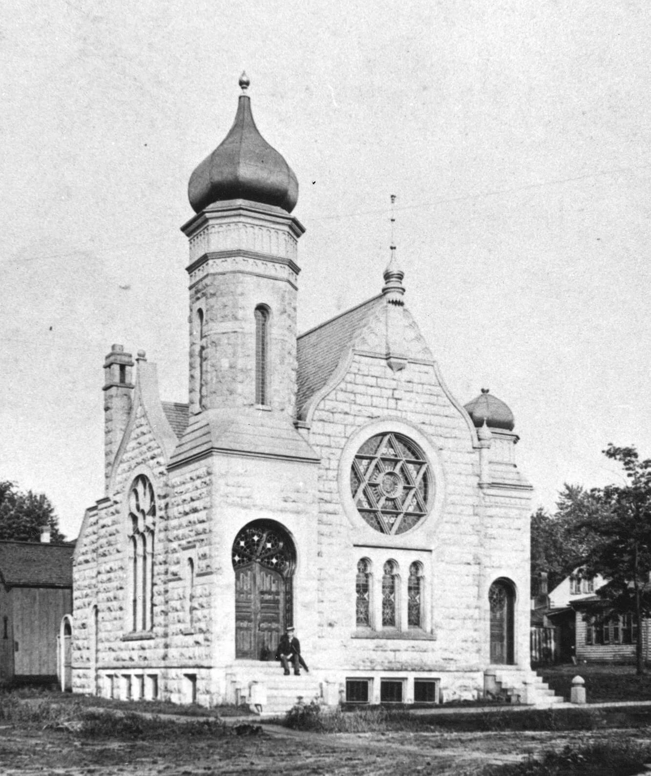 Exterior of a cathederal with a large round Jewish star stained glass window in the front, and a tall onion-dome topped tower.