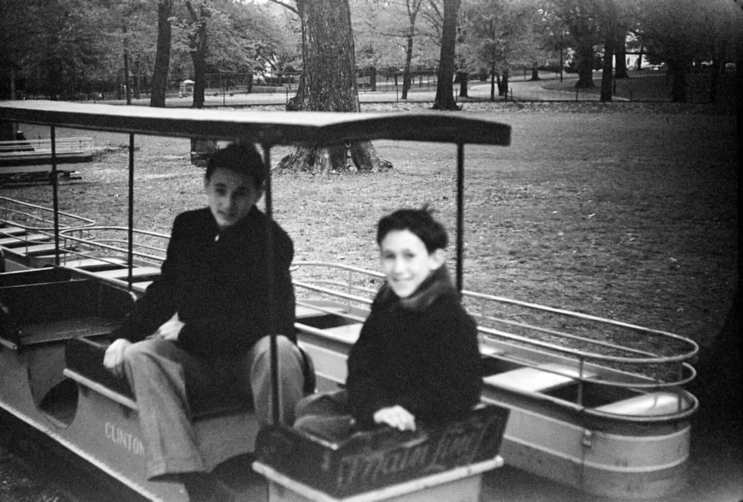 Two boys ride a miniature train in a park.