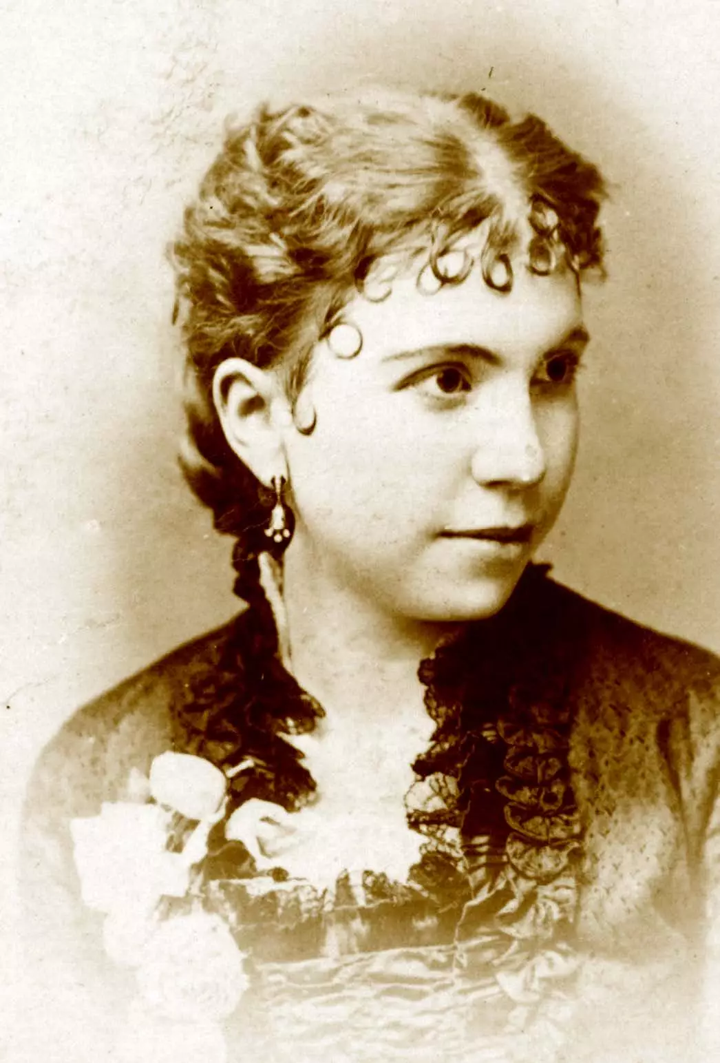 Young light-skinned woman looks to the right. She has curly hair that is pulled back except for a dozen or so short curls that are carefully laying on her forehead.