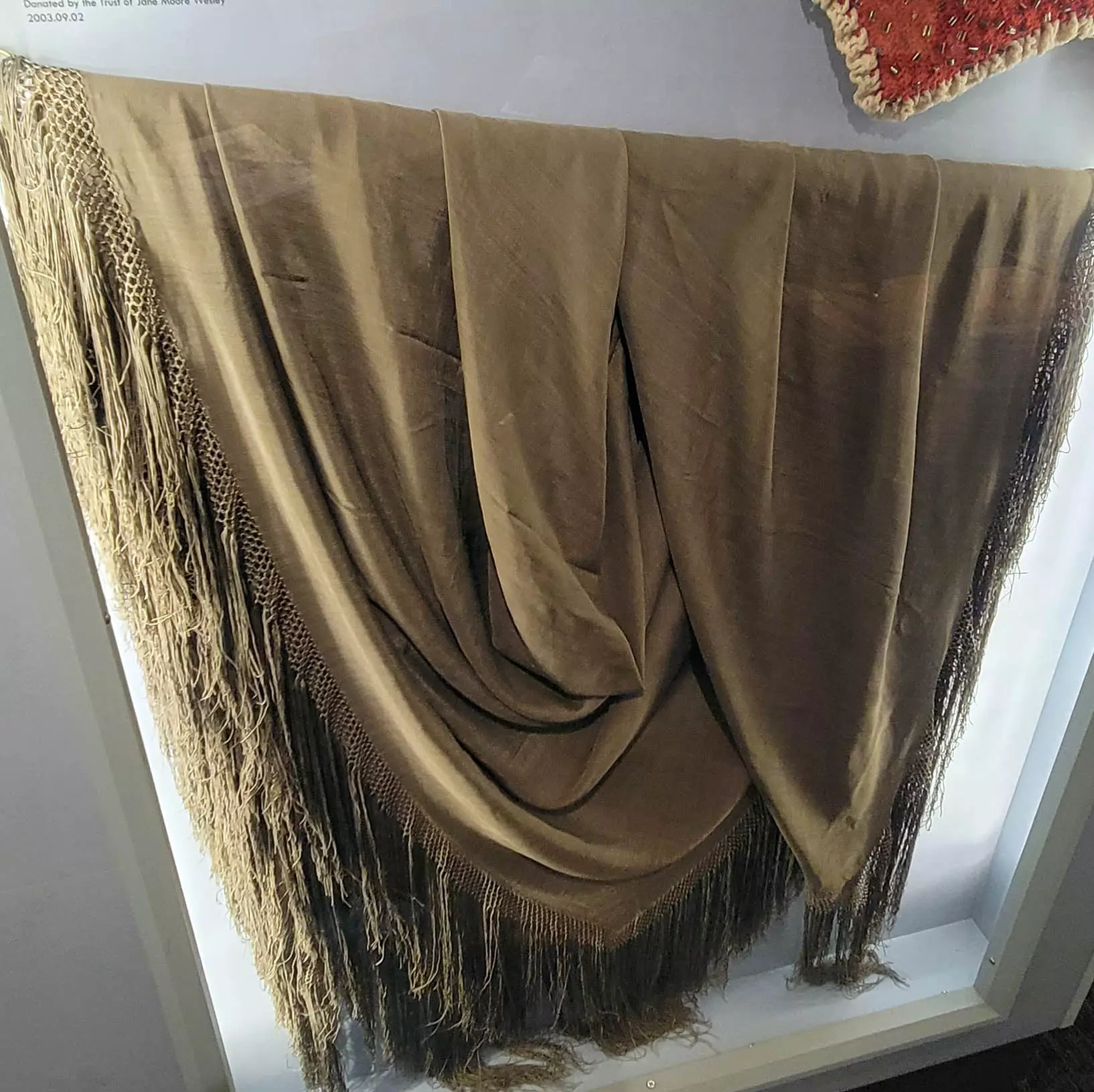 Photo of a beige fabric shawl with long fringe at the edges.