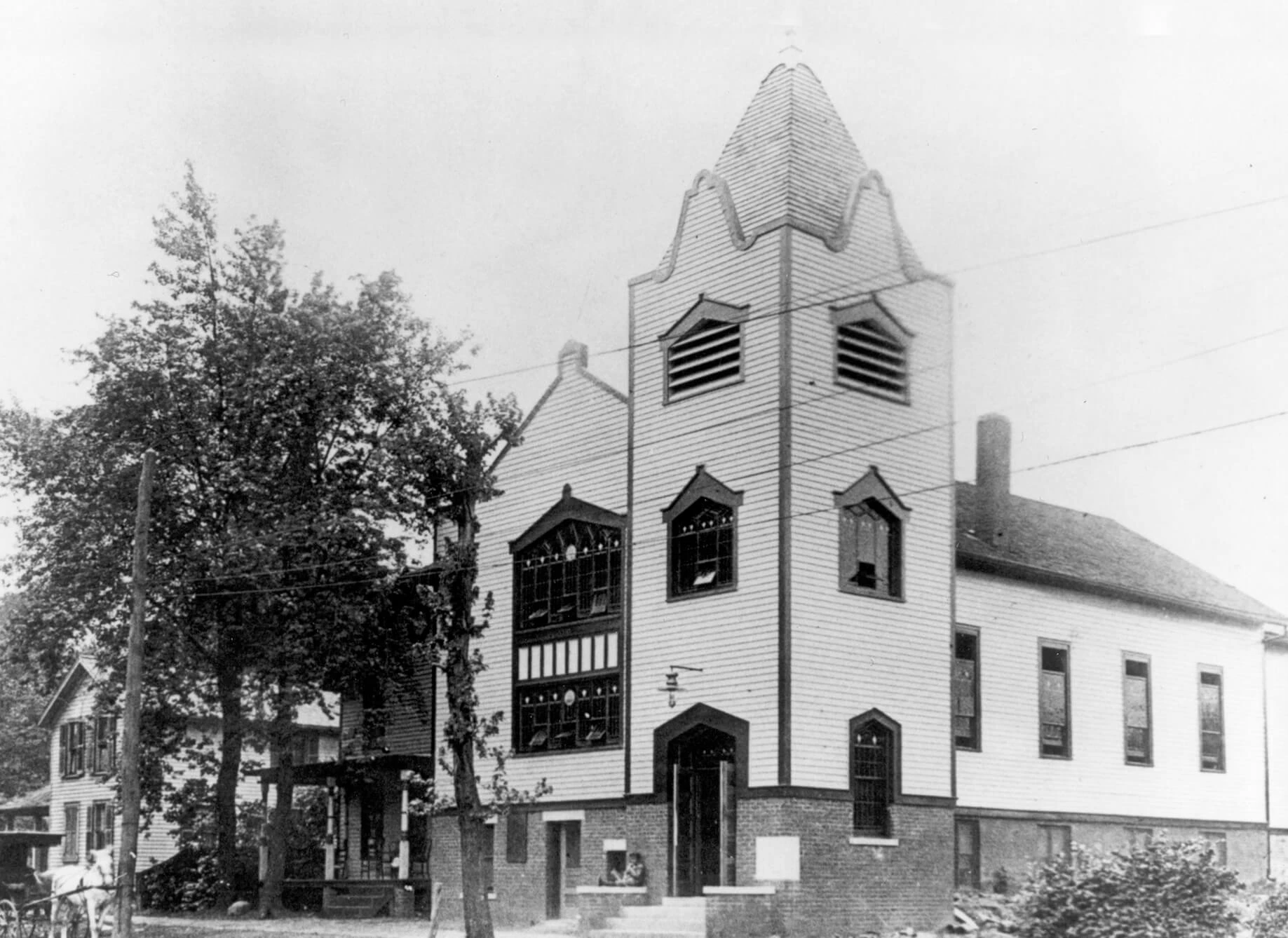 a one-story church with a three-story bell tower in front and steps leading up to the front door.